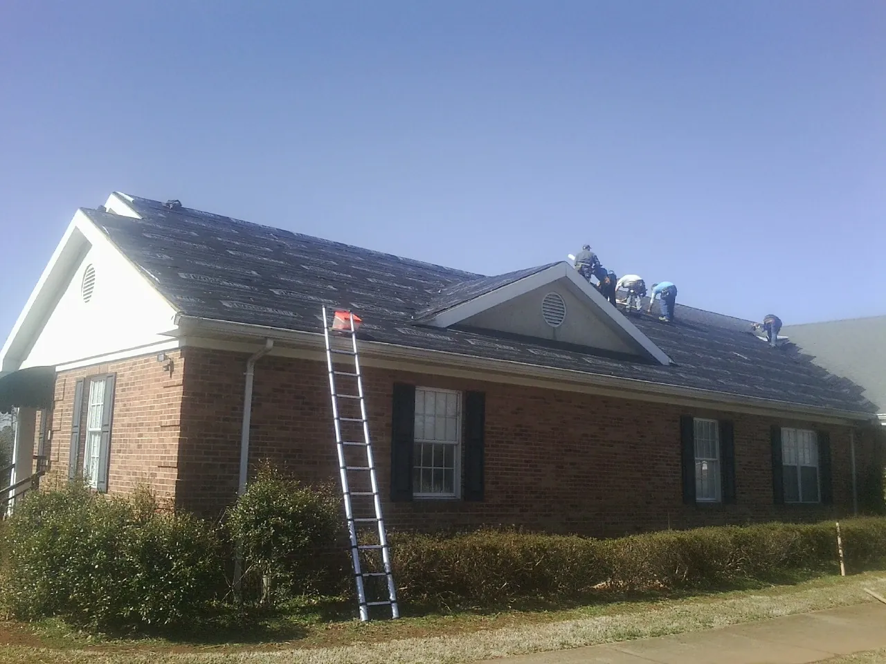 Crew tearing shingles off a brick ranch roof with a ladder set — Metal Roof Repair work by our crew in Marshall